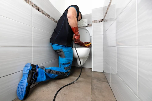 Plombier qui effectue un débouchage WC avec un furet électrique.